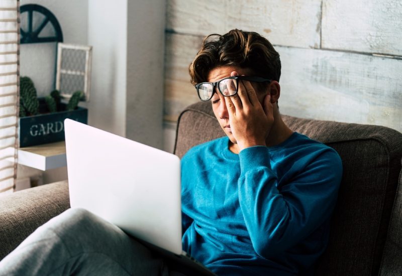 Feeling Stressed This Semester? These Strategies Can Help 1 A young teen in glasses and a blue top rubbing their eye from exhaustion while sitting with their laptop on their lap.