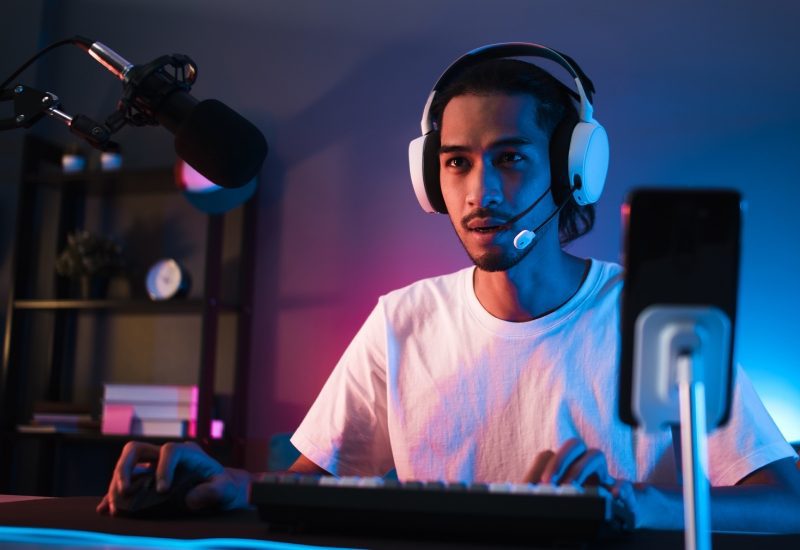 Solid Tips for Fixing Your Latency or Lag Issues in Matches 1 A young man sitting at a desk in a dark room lit by dim purple lights. He is streaming content to an online audience.