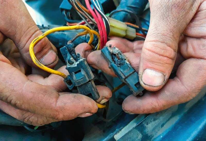 How To Prevent Short Circuits in Your Vehicle 1 A male car mechanic's dirty hands holding two charred automotive wires with melted casing after a short circuit.