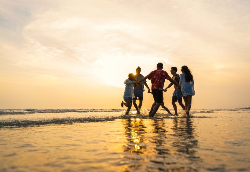 Fun Activities To Do Before Your Orlando Vacation Ends 1 A diverse group of teens holding hands in a circle on the beach. They splash the water at their feet as the sun sets.