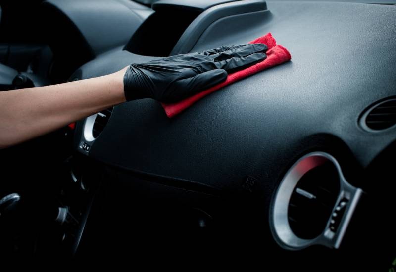 Car Interior Detailing Basics: Things To Know 1 Someone wiping the inside of their car with a microfiber cloth. They're wiping the dash in a pair of gloves.