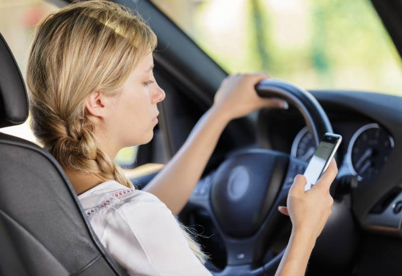 Understanding the Dangers of Distracted Driving 1 A teenage girl drives a car with one hand on the steering wheel, looking down at her smartphone in her right hand.